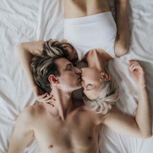 A couple sharing an intimate kiss while lying side by side on a bed.